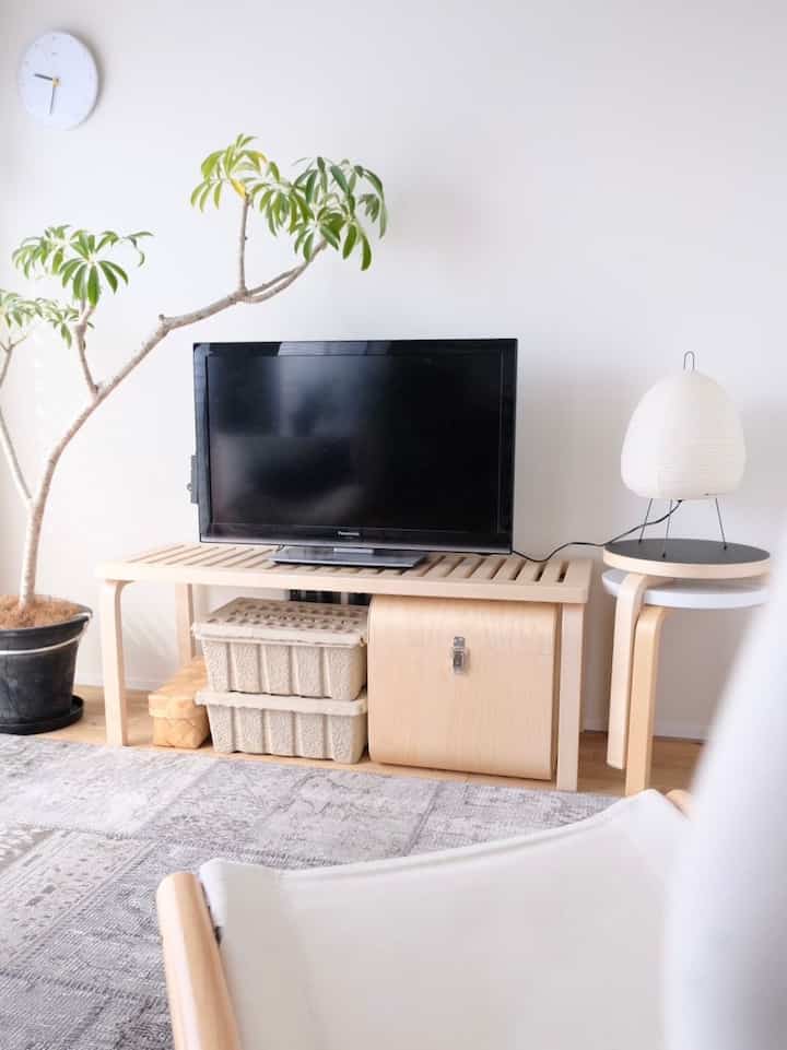 白い壁とナチュラルな木目調家具、テレビ台と植物が配置されたシンプルなリビング