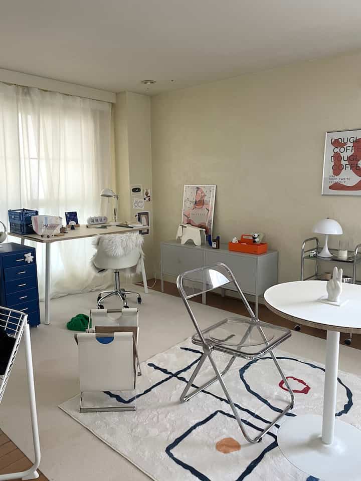 ベージュと白を基調とした1DKのリビング兼ワークスペース、透明な椅子とデスク、アートが配置されたモダンで清潔感のあるインテリア