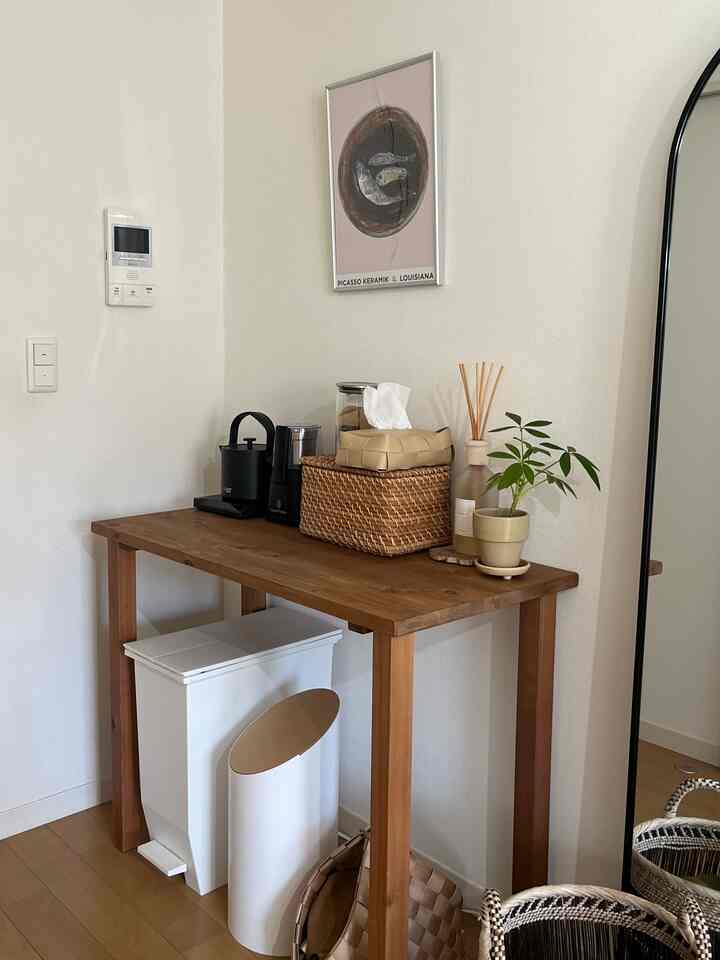 ナチュラルな木目調のテーブルが壁に配置され、おうちカフェ用のコーヒーグラインダーやディフューザー、観葉植物が置かれたシンプルな一人暮らしのキッチンスペース