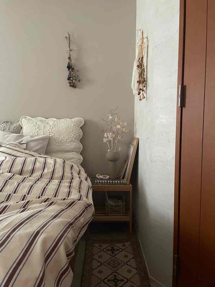 ベージュとブラウンの色調の寝室、ストライプの掛け布団カバーとナイトテーブル、ナチュラルな装飾が配置された雰囲気のあるインテリア