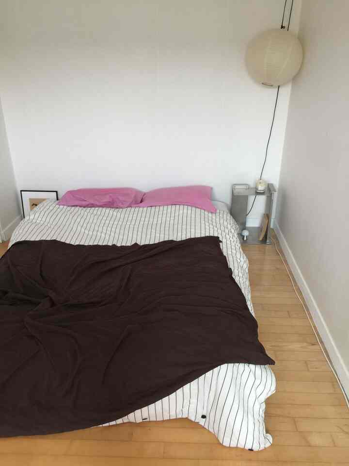 白い壁と茶色のベッドカバーが調和した寝室、ピンクの枕とナイトテーブル上のキャンドルがある整った空間