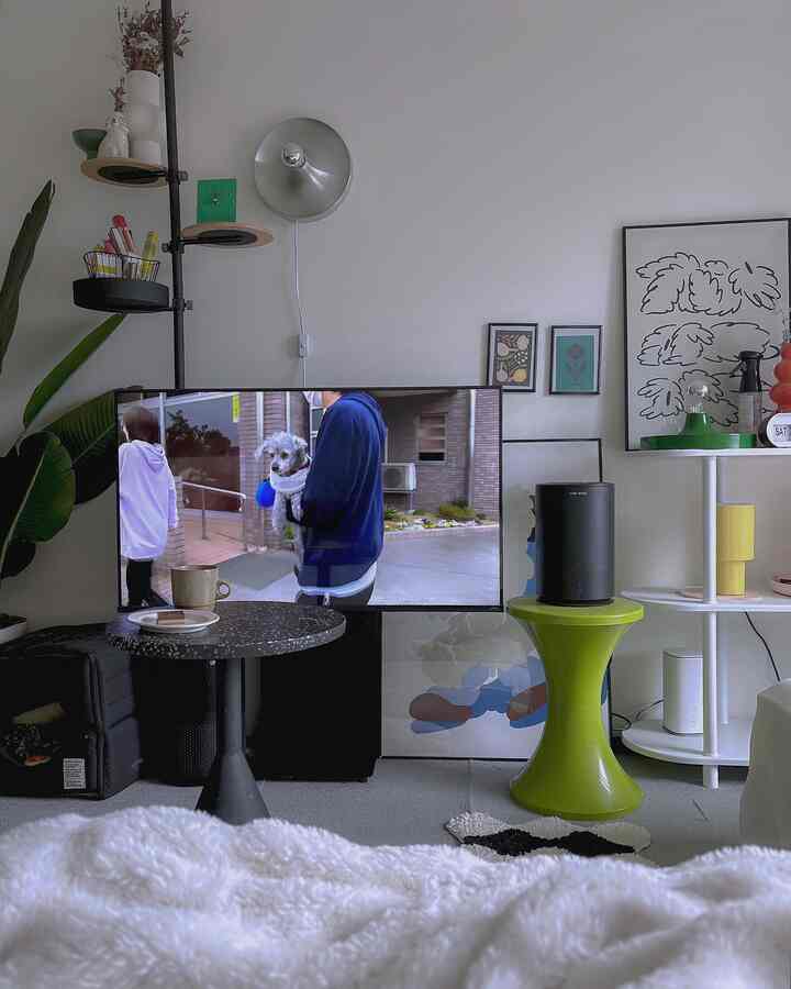 A white and green toned bedroom featuring a TV and side table centered with a clean and modern interior