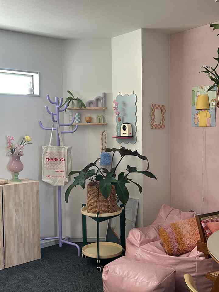 白とピンクのパステル調のリビング、ビーズクッション、コートハンガー、植物が配置された雰囲気のある空間
