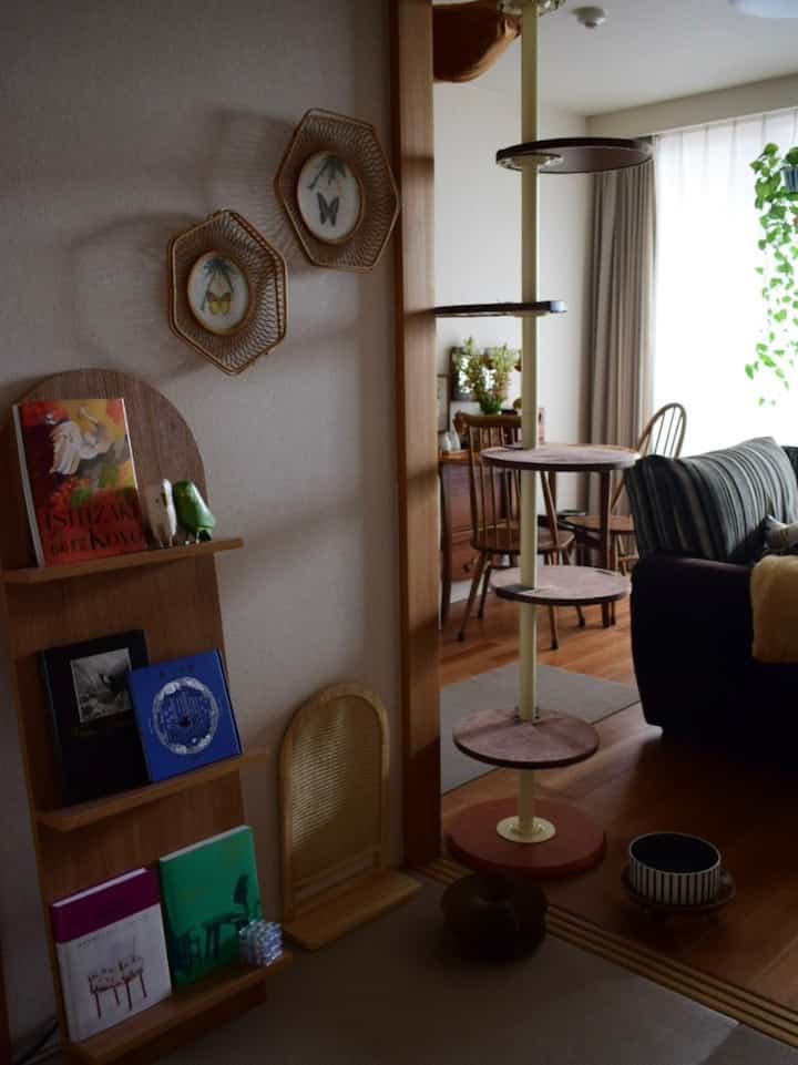 ナチュラルな木目調とヴィンテージ家具が配置されたリビング、猫用キャットタワーと爪とぎが見える印象的な空間