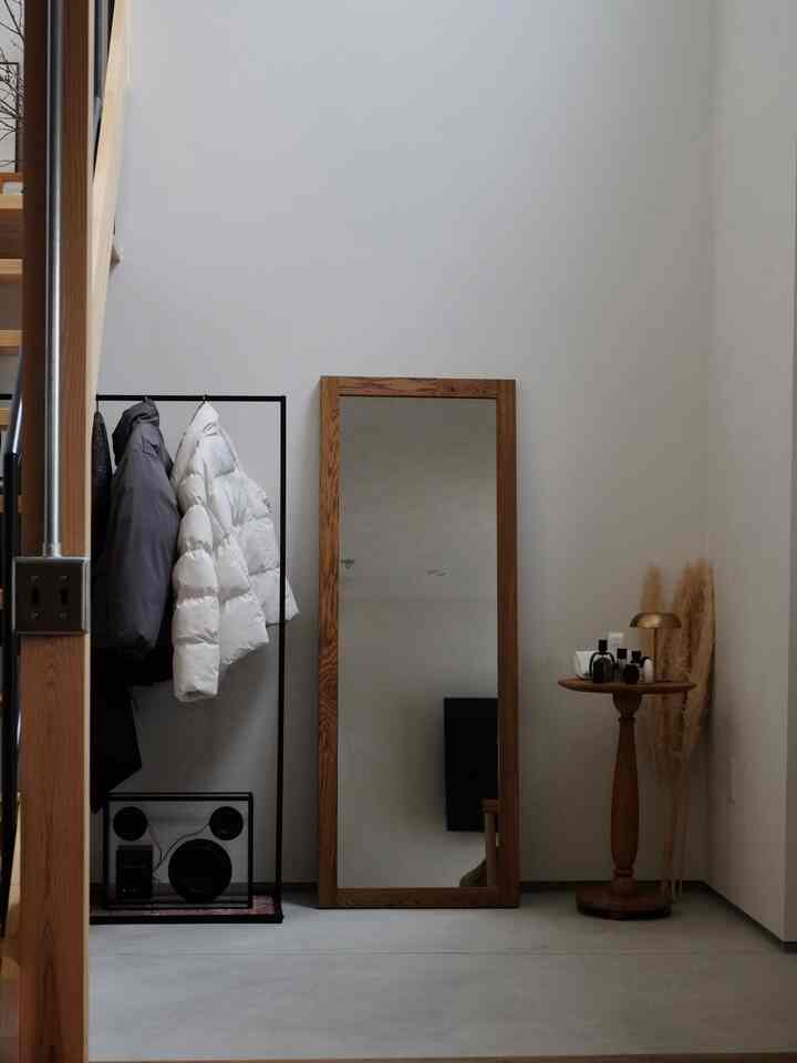 ナチュラルカラーの玄関空間にブラックのアイアンコートラックと木製フレームの鏡、丸い木製ペデスタルテーブルが配置されたシンプルで落ち着いたインテリア