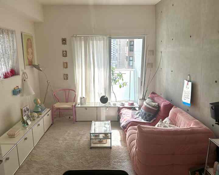 明るい自然光が差し込むピンクのソファが印象的なコンパクトなリビング、白いサイドボードとベージュのラグが配置された雰囲気のあるインテリア