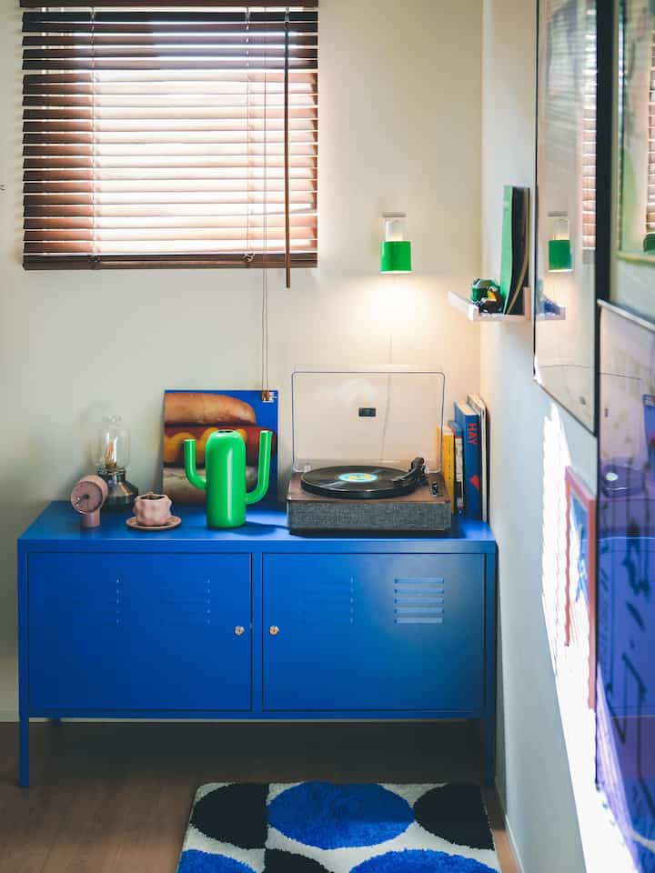 明るい青色のキャビネットがあるコンパクトな部屋、ヴィンテージのレコードプレーヤーと緑の花瓶が配置されたレトロな雰囲気のインテリア