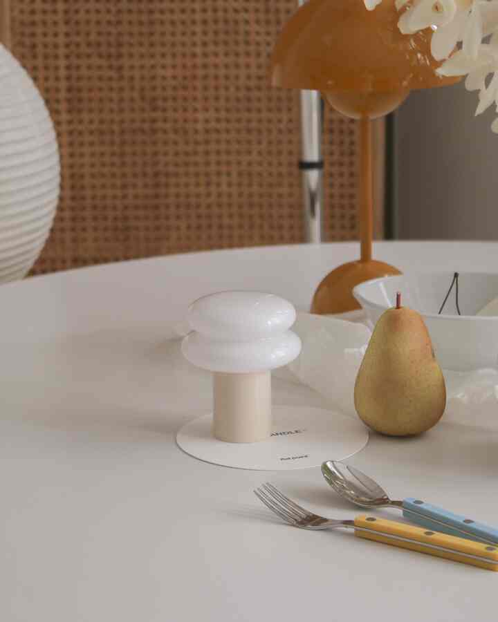 Natural brown and white toned kitchen table featuring a mood lamp, cutlery, and fruit in a simple interior