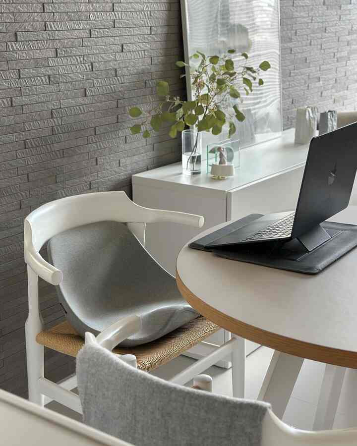 Modern workspace with gray brick wall and white furniture, featuring a round table and laptop set up for remote work