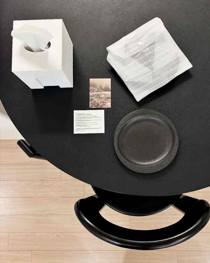 黒い丸テーブルの上に白いティッシュケースと黒いテクスチャーの皿が置かれたキッチン空間、洗練されたモダンな雰囲気