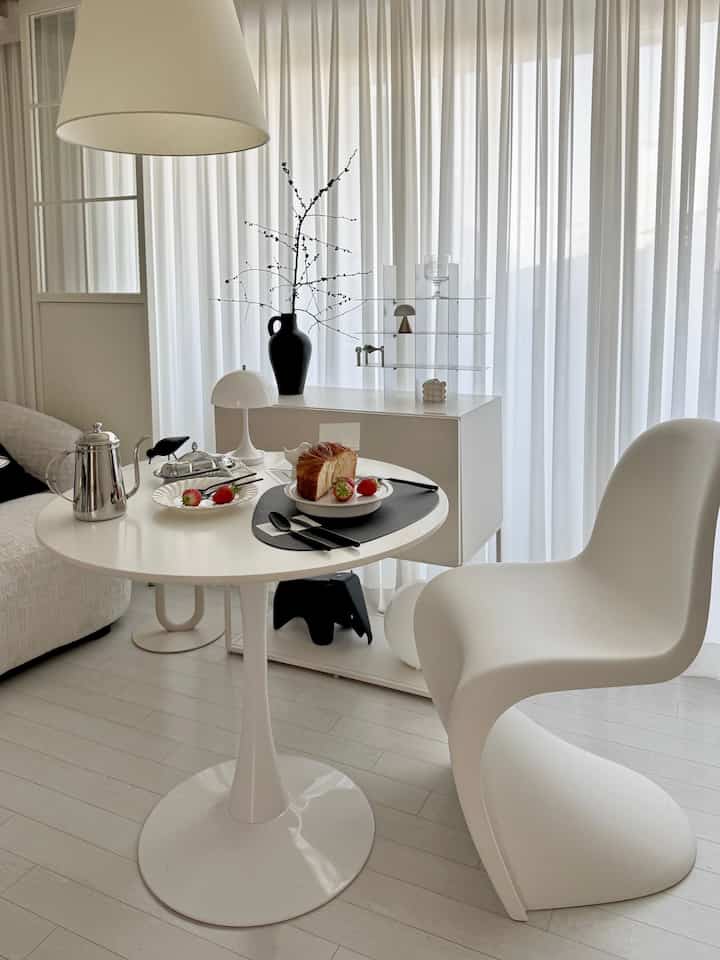 Bright white toned living room featuring a curved chair and round table with cutlery and dessert, embodying a simple and modern interior