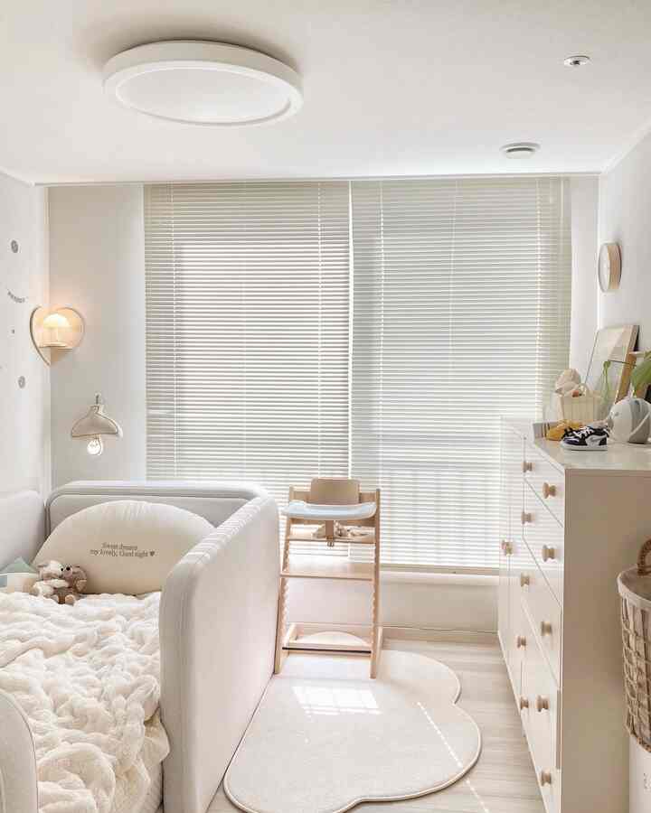 明るく落ち着いた白を基調とした赤ちゃん部屋、ベビーベッドや洋服ダンス、ラグ、ベビーチェアが配置された温かみのあるインテリア