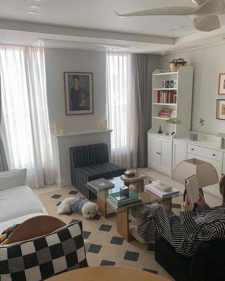 白とベージュの色調のリビング、白いソファとベージュのラグが配置されており、犬と読書する人がいるシンプルな空間