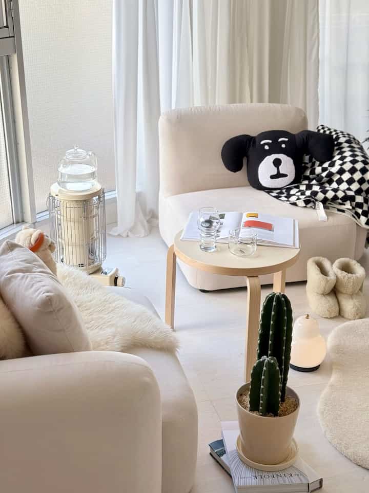 白とベージュの色調のリビング、アイボリーのアームチェアと木製のテーブル、観葉植物のサボテンが置かれた雰囲気のある空間