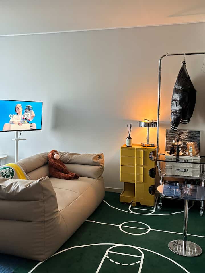 ベージュのソファとバスケットボールコート柄のグリーンラグが配置されたリビング、モダンでくつろげる雰囲気