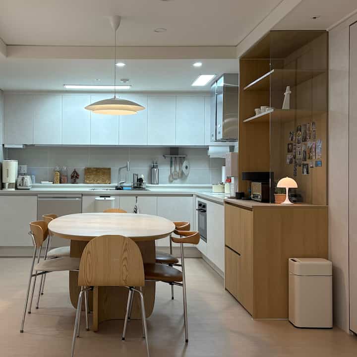 ホワイトとブラウンの色調のキッチンとダイニング、中央に丸いダイニングテーブルと木製の椅子が配置された自然でモダンな雰囲気のインテリア