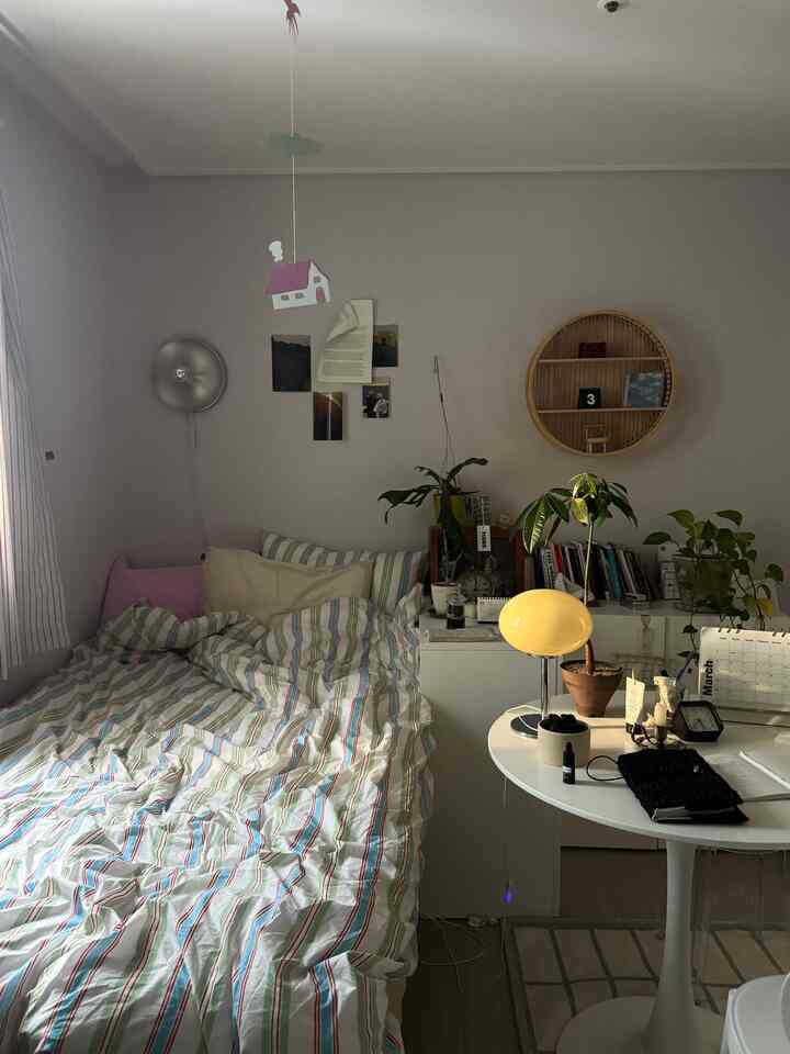 ホワイトとウッドトーンが調和した狭い寝室、ベッドと植物、テーブルランプが配置された落ち着いた空間