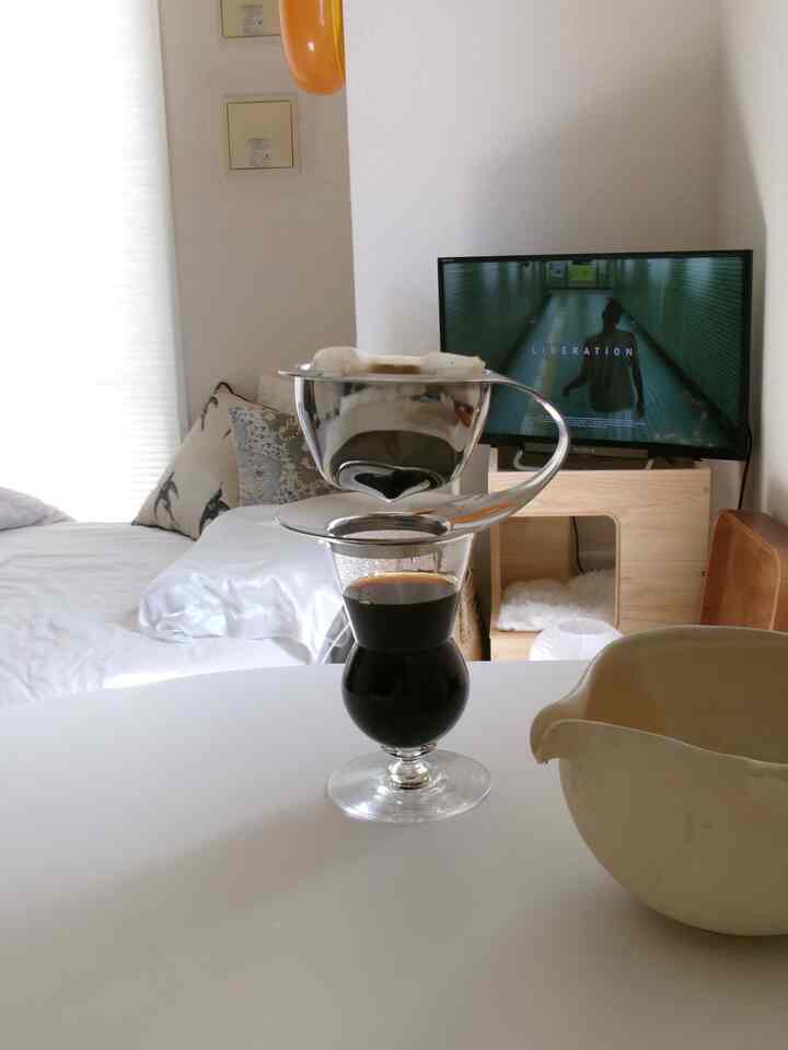 White-toned studio bedroom with a hand-drip coffee set and glass on a central round table in a minimalistic interior