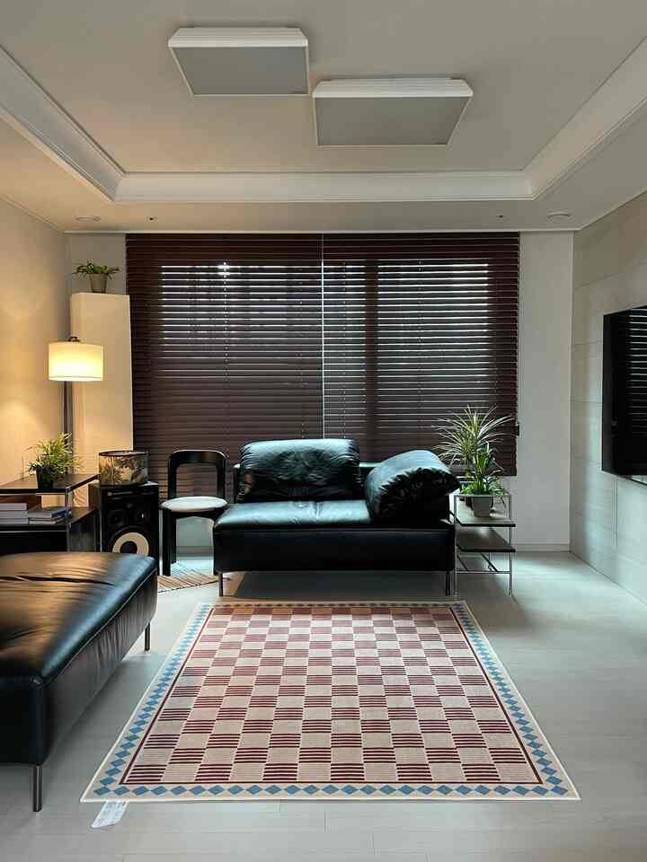 ウッドトーンとブラックを基調としたリビング、中央にレザーソファとパターンラグが置かれ、サイドにフロアランプが配置された雰囲気のあるインテリア