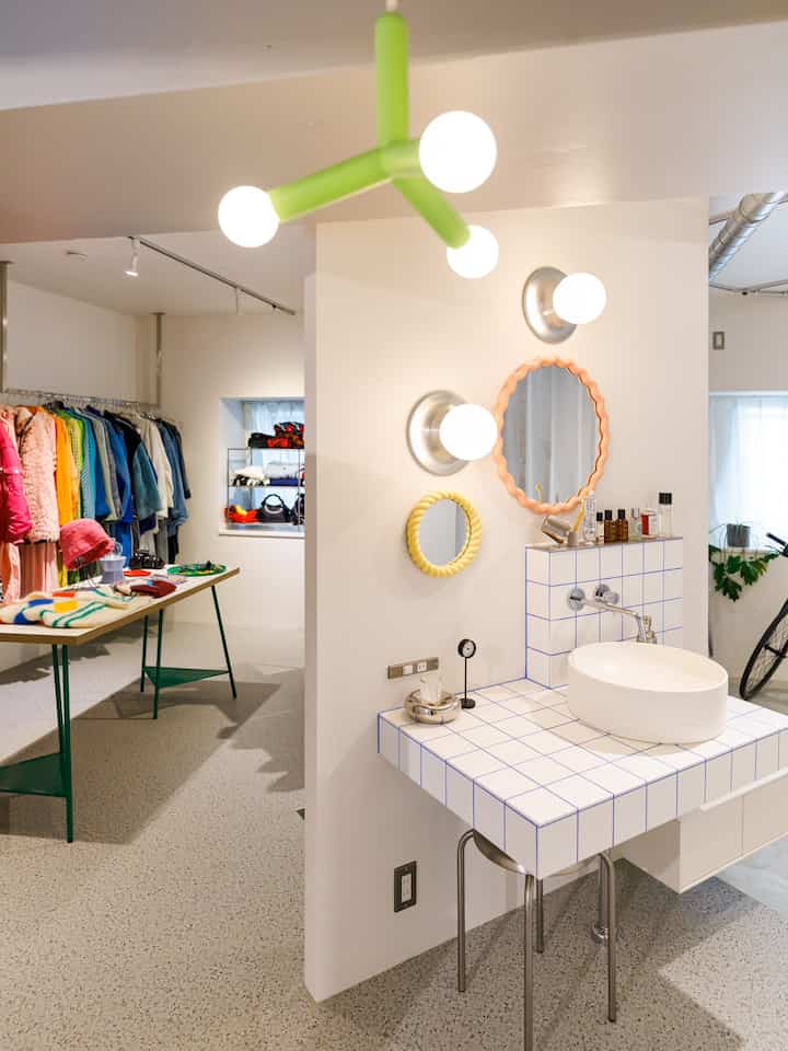 白い壁と床、タイル製の洗面台にカラフルな黄色とオレンジの鏡が配置された、洗面所とクローゼットがつながる印象的なレイアウトのインテリア