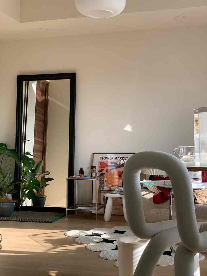 白い壁と木目調の床が際立つ二人暮らし向けのリビング、モダンなブラックフレームの鏡と観葉植物が配置された空間