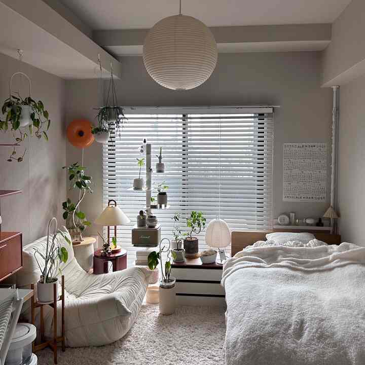 ナチュラルな色調の寝室、ウッドブラインドと植物が配置された落ち着いた雰囲気のインテリア