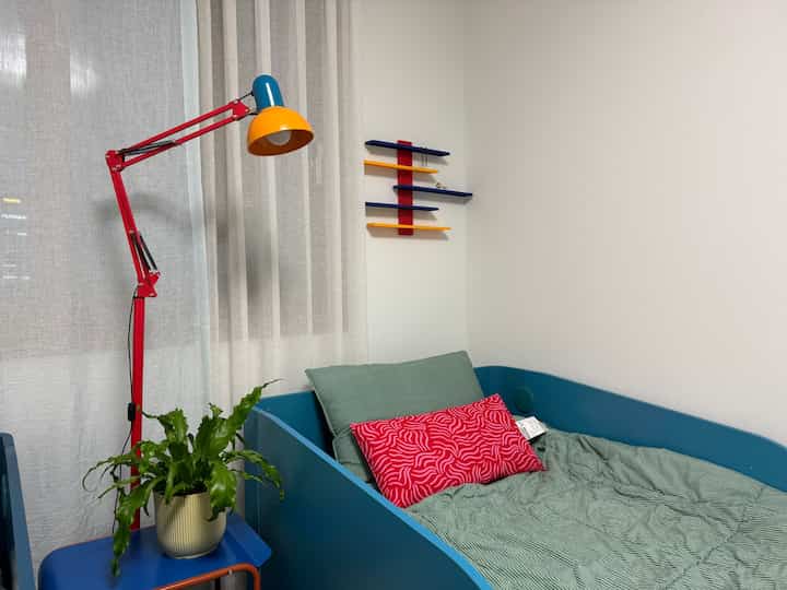 ブルーとレッドの色調の子供部屋、パステルグリーンのベッドとカラフルなランプが配置されたシンプルな空間