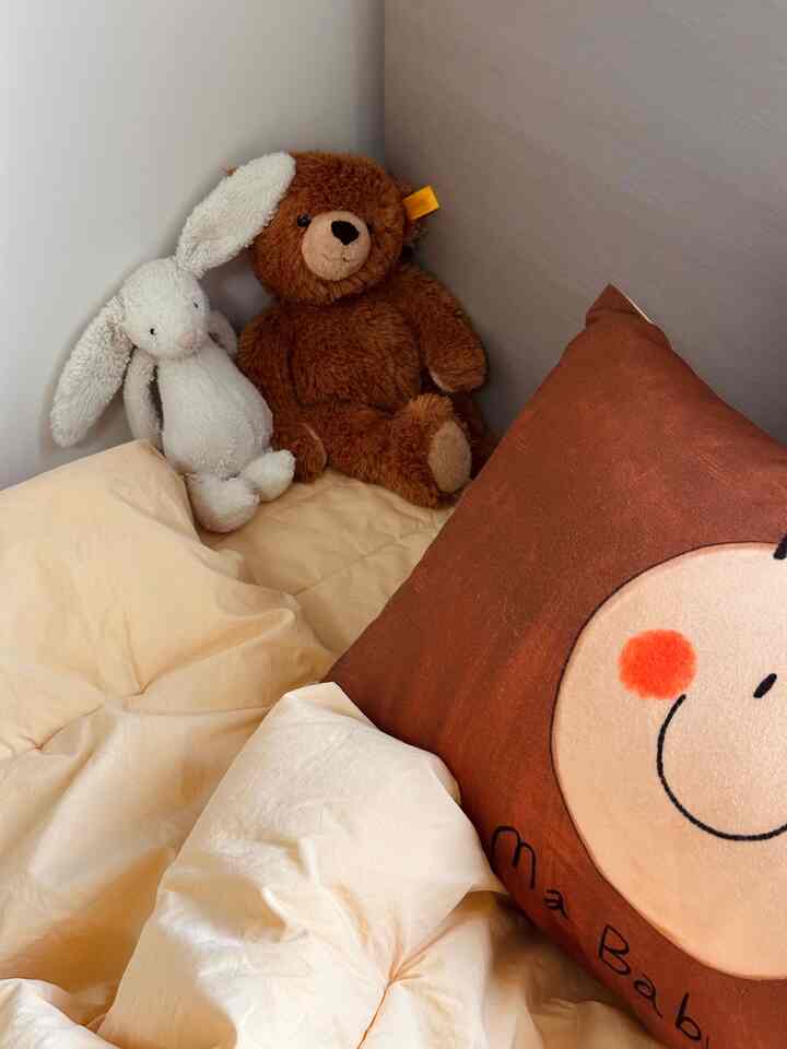 黄色と茶色の色調の子供部屋のベッド、ぬいぐるみとかわいいクッションが置かれ、温かみのある雰囲気のインテリア