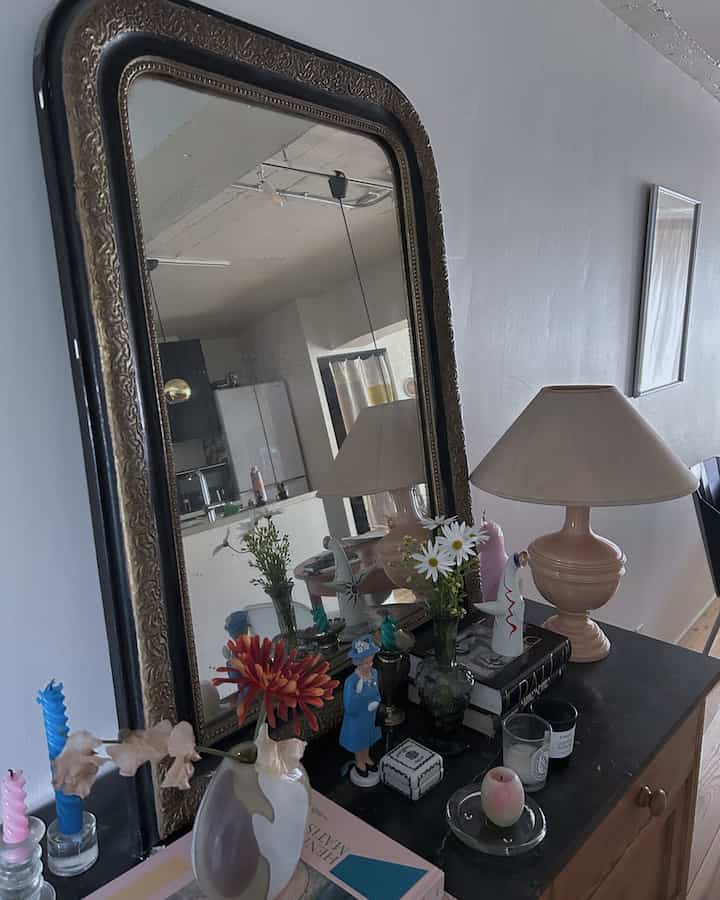Natural beige-toned living room featuring a vintage chest, mirror, floral vases, and candles creating a cozy atmosphere