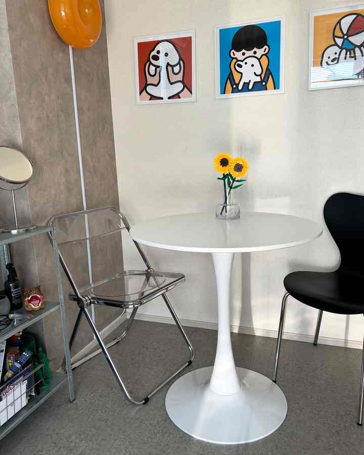 White and gray toned small clean studio apartment cafe-style space featuring a round table, transparent chair, and wall art