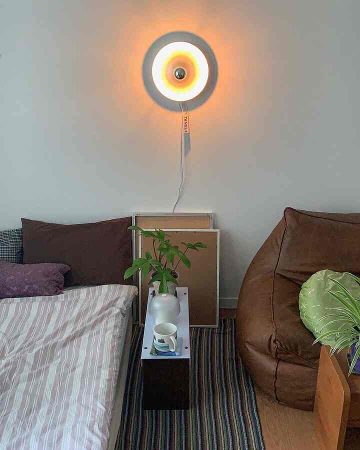 ベージュとブラウンのトーンでまとめられた小さな寝室、ベッドとビーンバッグ、サイドテーブル、植物が配置された自然な雰囲気のインテリア