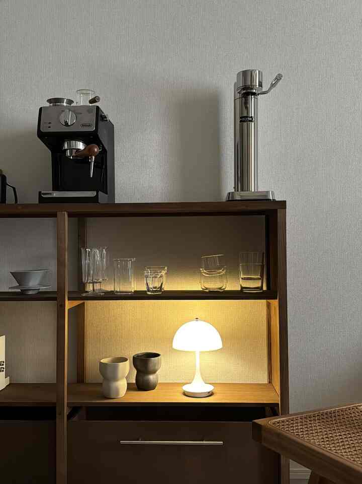 白い壁と木目調の棚があるおうちカフェ空間、中段の棚にはムード照明とカップが配された雰囲気のあるインテリア