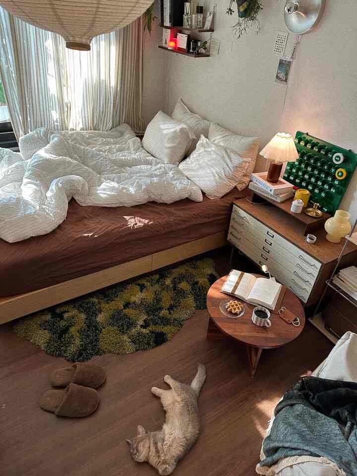 ブラウンの床と白い寝具の寝室、猫と丸いコーヒーテーブルが配置された雰囲気のある空間