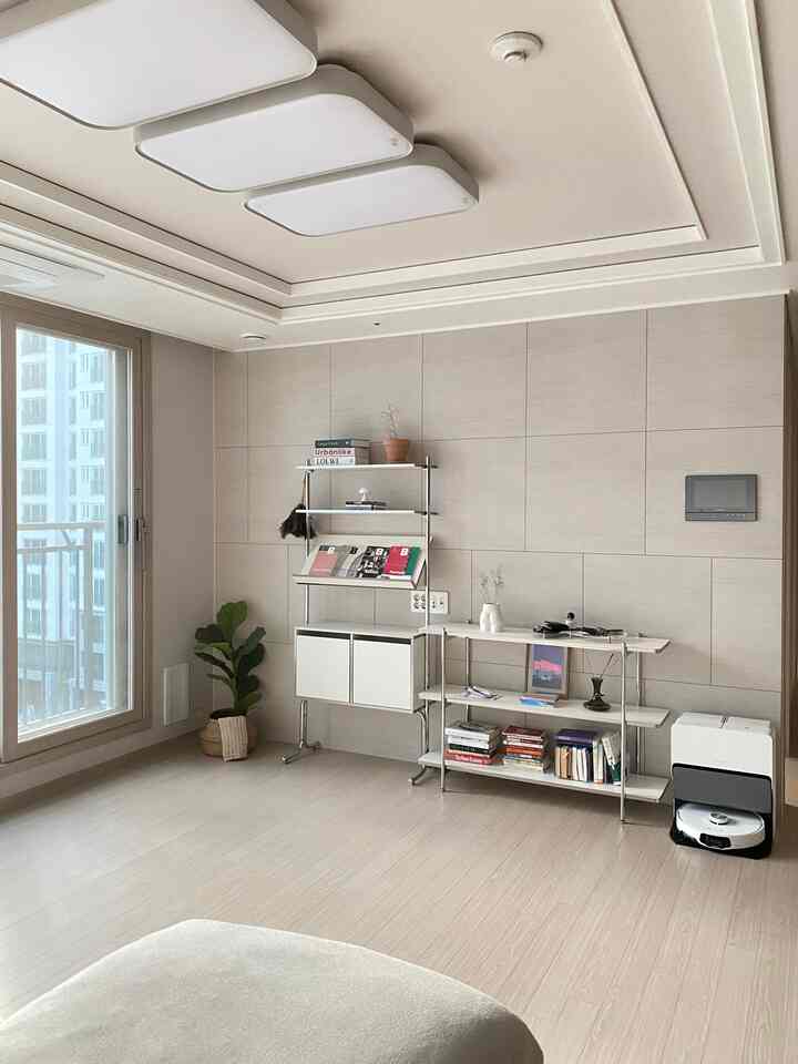Beige and white toned living room featuring minimal natural bookshelves and a plant with a clean atmosphere