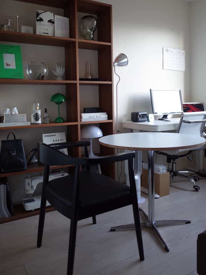 白い壁と木目調の本棚があるホームオフィス空間、ラウンドテーブルと黒い椅子が配置されたモダンなインテリア