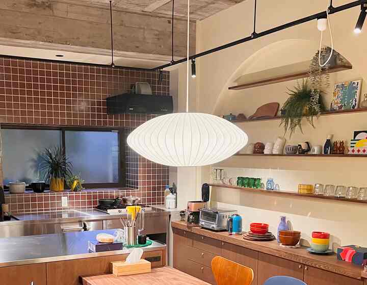 Natural wood tone and brown tiled kitchen featuring a large white pendant light at center, mid-century modern style space