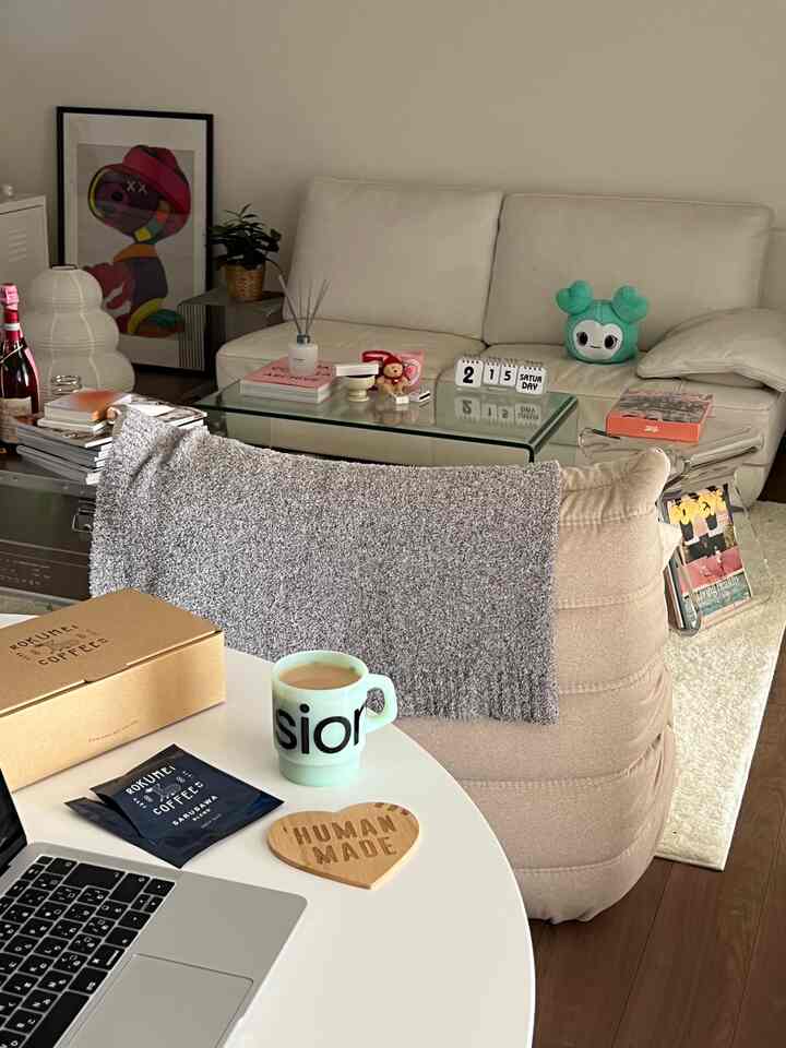 Beige and white toned living room featuring a beige stool, white sofa, and round table with coffee and laptop creating a cozy home cafe vibe