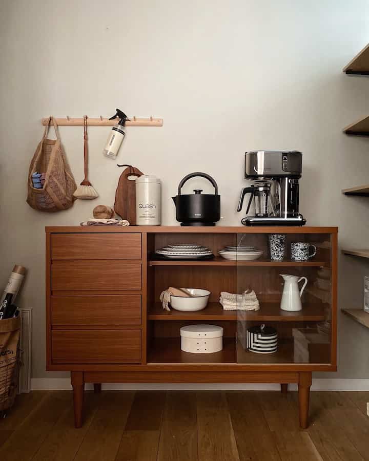Natural wood-tone kitchen cabinet featuring a black electric kettle and silver coffee maker in a mid-century modern styled space