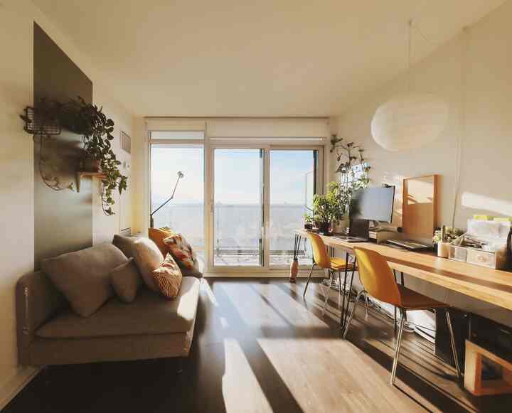 Warm wood tone and natural color living room featuring large desk by window and gray sofa in modern style
