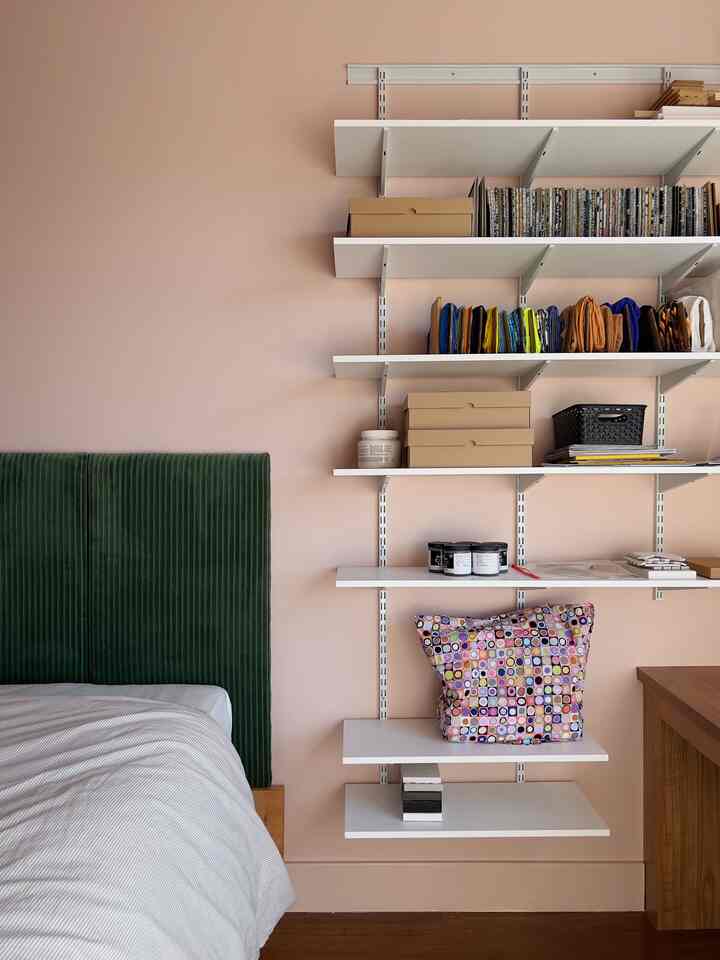 Beige-walled bedroom with green headboard bed and white open shelving mounted on wall, cozy eclectic atmosphere