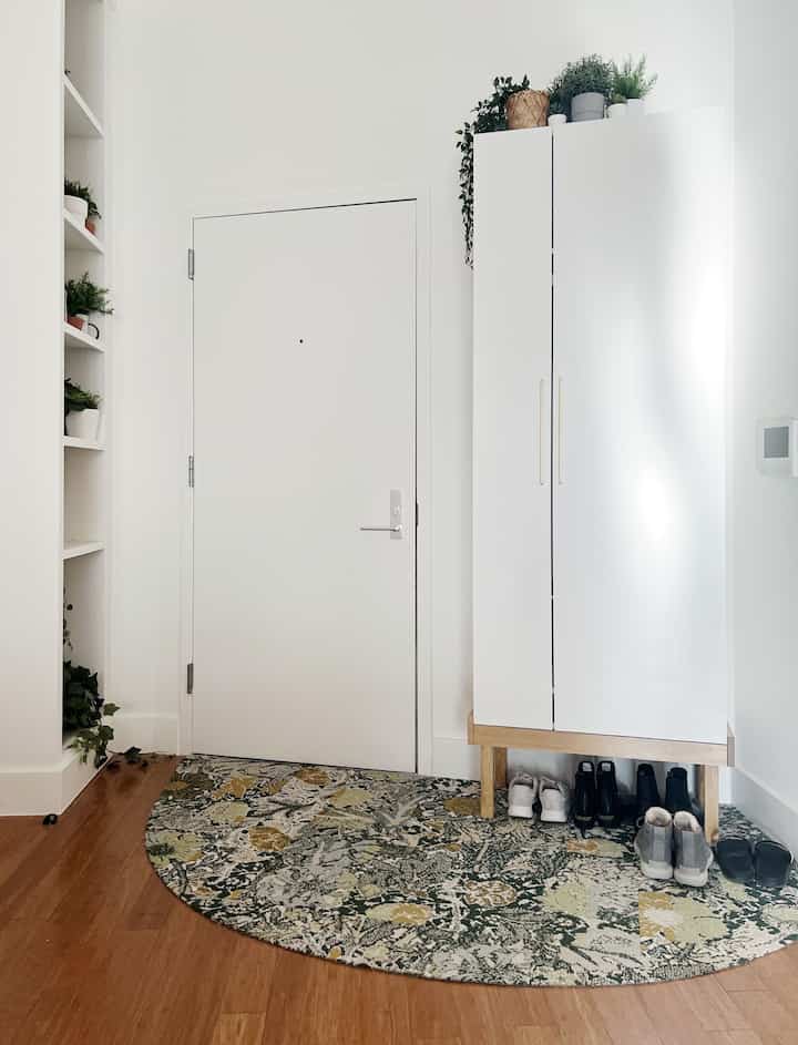 White and green toned entrance featuring a white storage cabinet, plants, and shoe storage in a clean setting