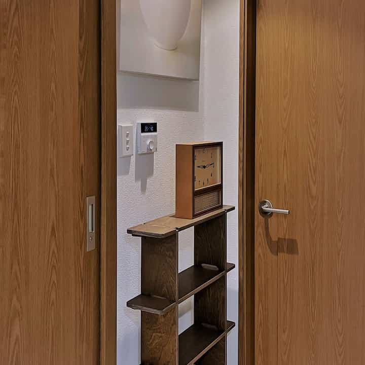 ブラウンの木製ドアと棚、ヴィンテージの時計が配置された白い壁の印象的な空間