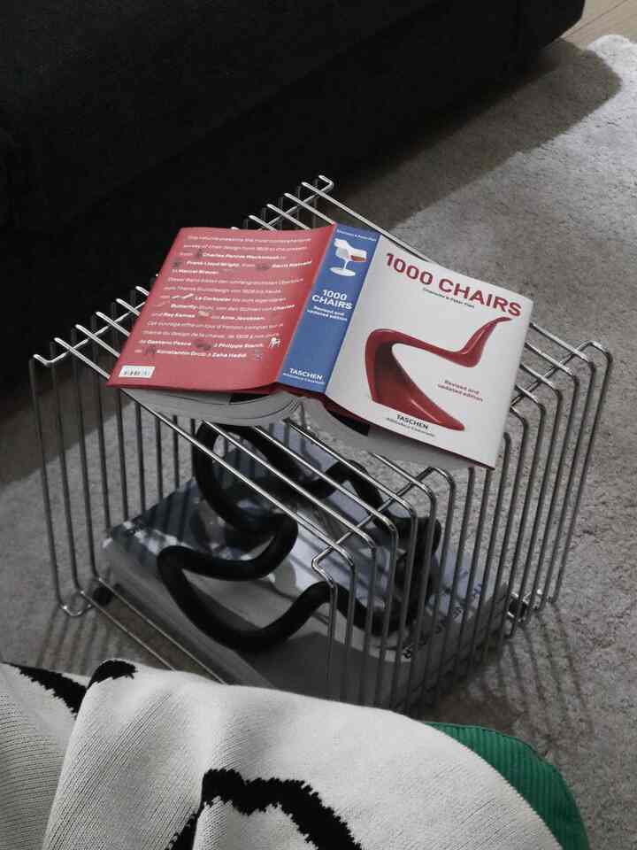 グレーのカーペットに黒いソファと金属製のワイヤーラックが置かれ、本が置かれたナチュラルな雰囲気のリビング