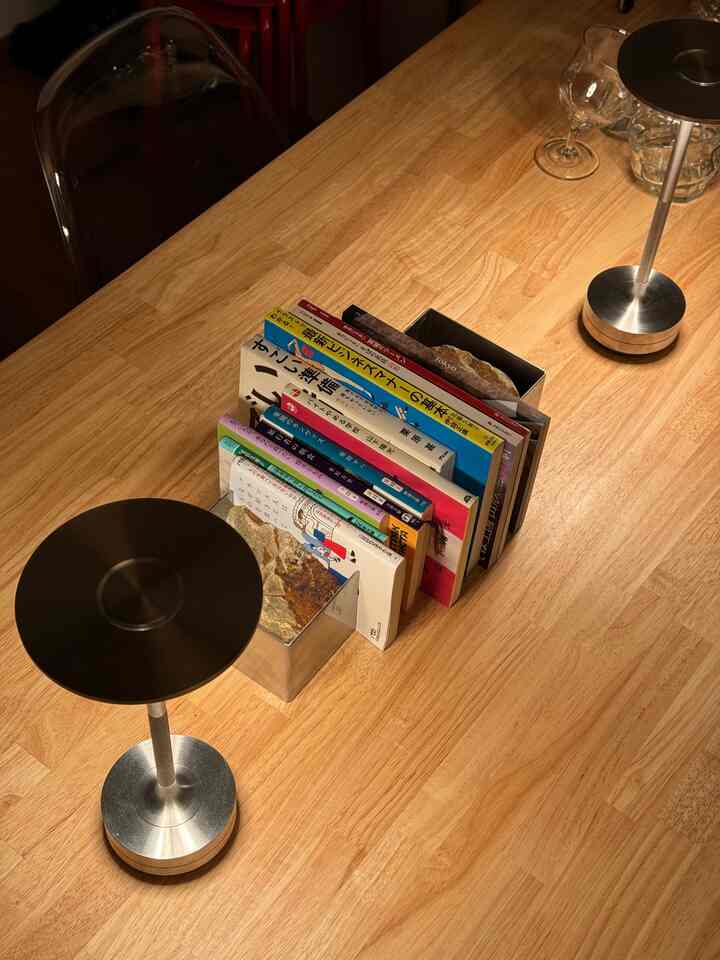 暖かいウッドトーンのダイニングテーブルに、透明な椅子とシルバーのテーブルランプが配置された一人暮らしの空間