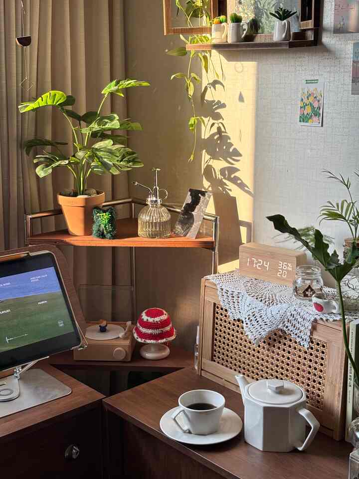 ナチュラルな色調のリビングルームのコーナー、植物とコーヒーカップが置かれたデスクと収納が調和した心地よいおうちカフェの空間