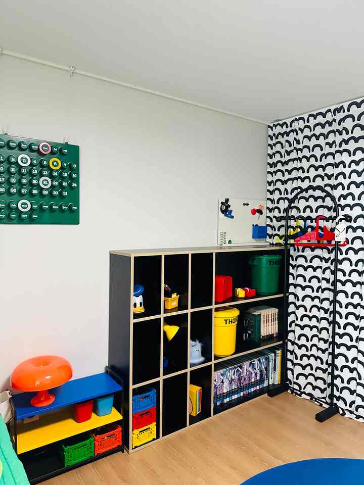 カラフルな子供部屋、ブラックと木目調の多機能収納棚とパターンカーテンが配置されたすっきりとした空間