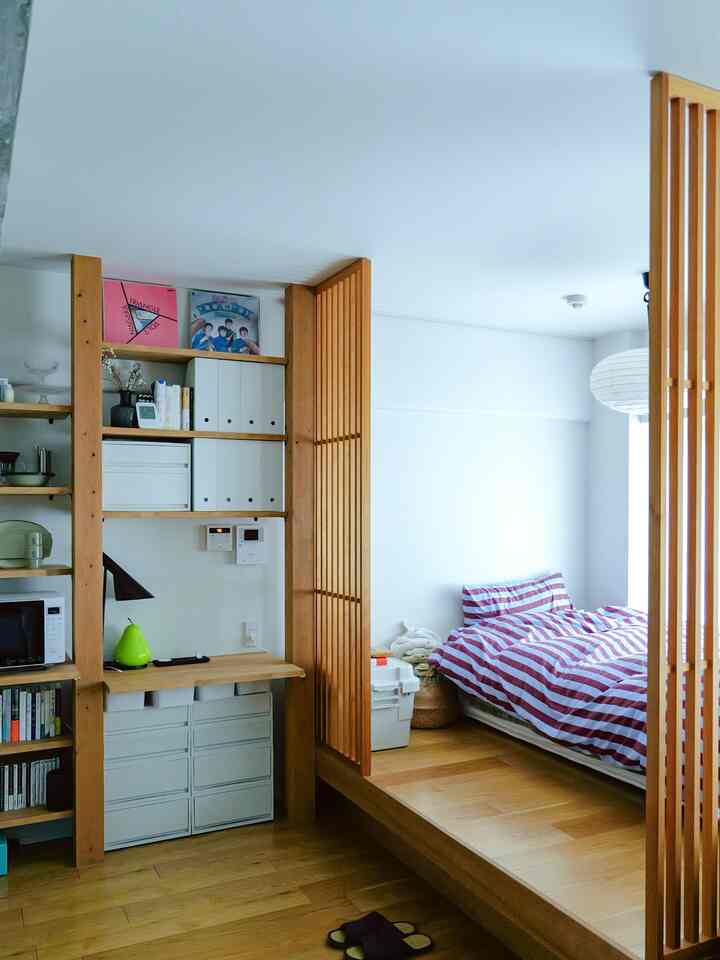白い壁と木目調の床、収納と小さな机が配置されたナチュラルな雰囲気の寝室