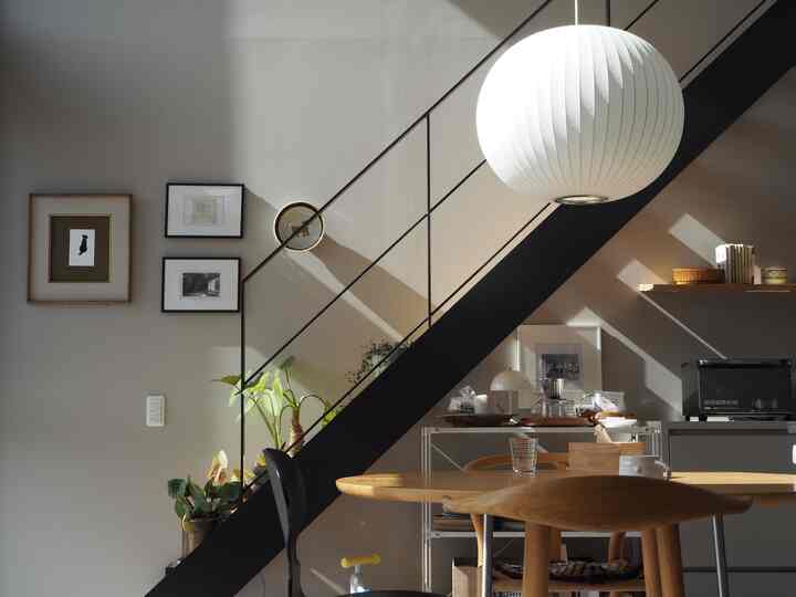 Dining room with white walls and natural wood table, featuring black stairs and art frames under abundant natural light