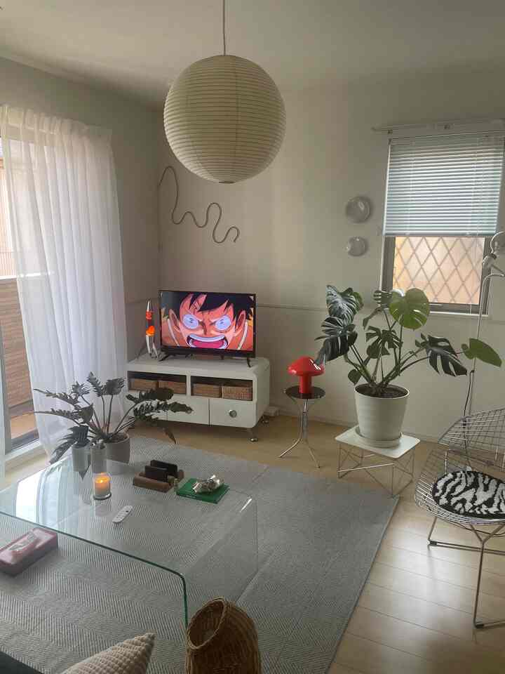 白と緑のトーンが調和するミッドセンチュリーモダンのリビング、ガラステーブルとワイヤーチェアが配置された雰囲気のある空間