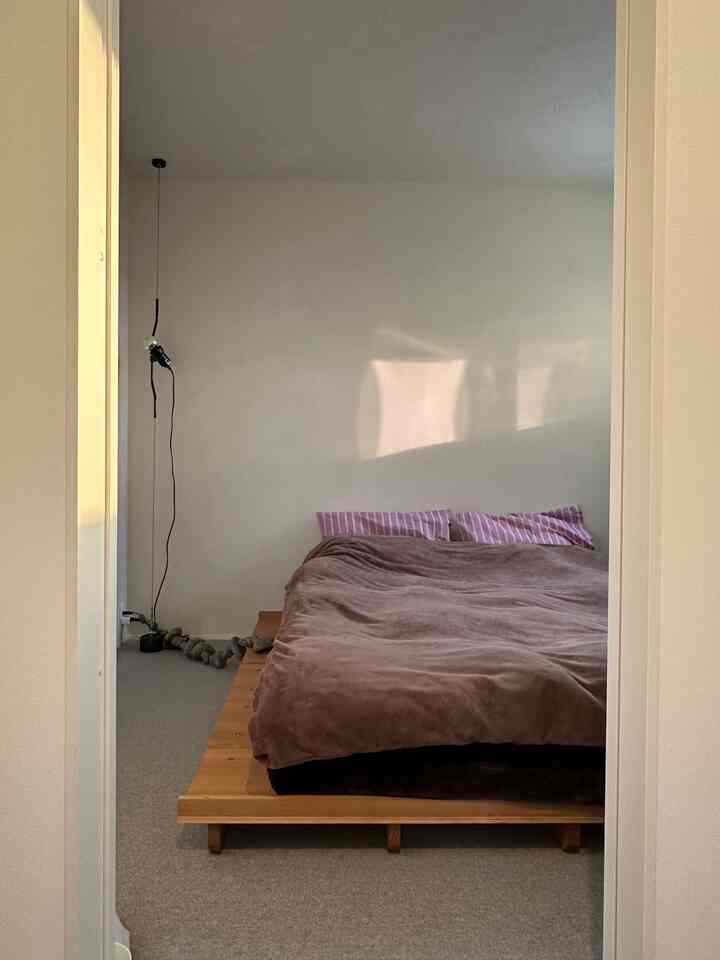Beige-tone bedroom featuring a wooden bed frame with pink striped pillows, showcasing a simple and natural atmosphere